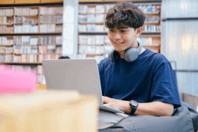 Un joven en una biblioteca frente a su laptop