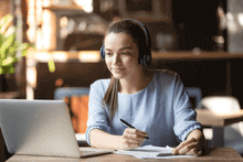 Mujer joven tomando nota sobre los cursos online que ve en su laptop