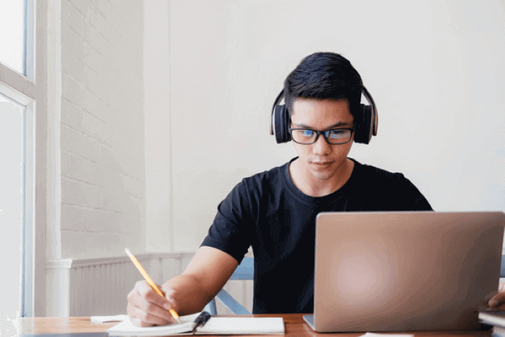 Un hombre joven con lentes y audífonos frente a una laptop tomando cursos de gestión en línea