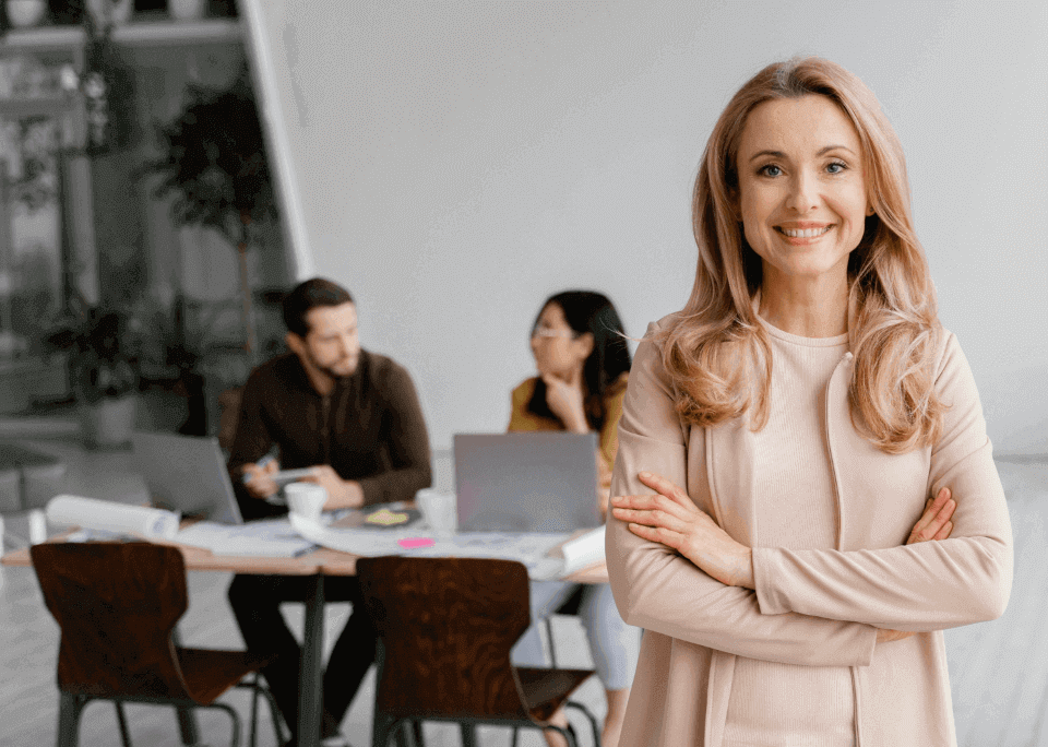 Mujer líder sonriendo por los buenos resultados en la evaluación 360 grados, detrás de ella colaboradores en una oficina