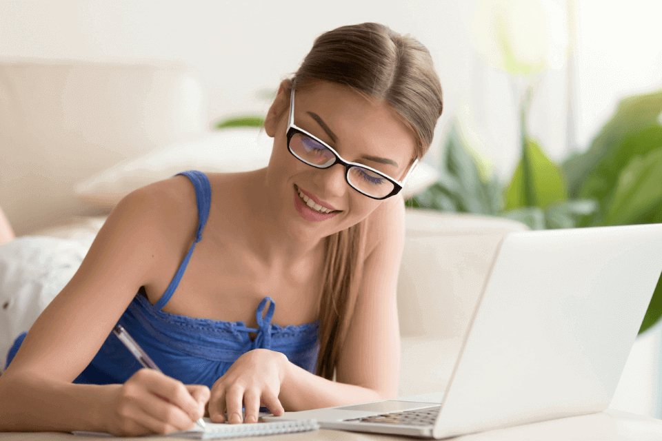 Una mujer rubia con lentes escribiendo notas del curso que sigue en la plataforma de capacitación online laboral
