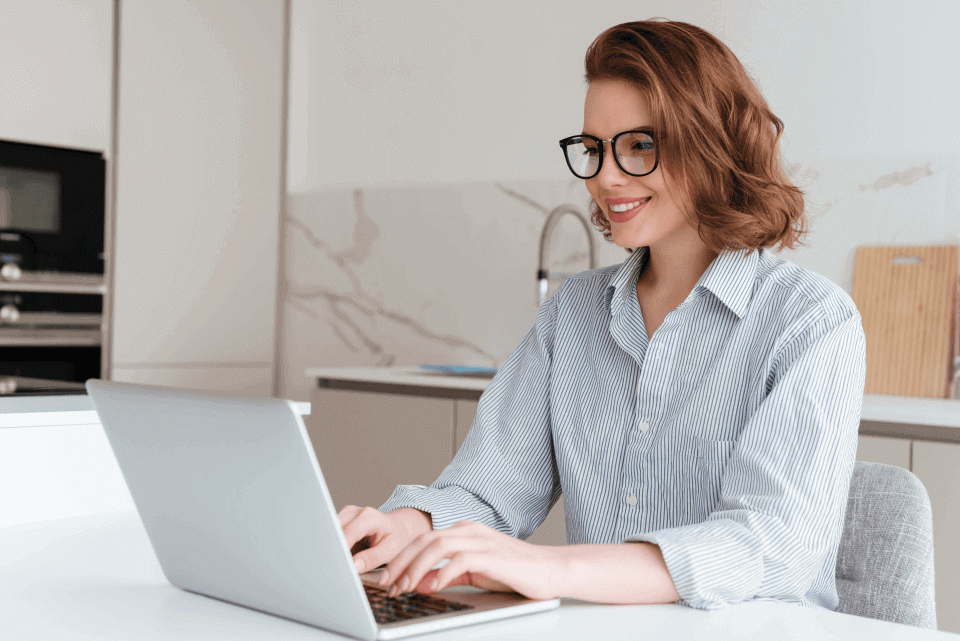 Mujer sonriente en su escritorio, revisando en su laptop la plataforma LMS