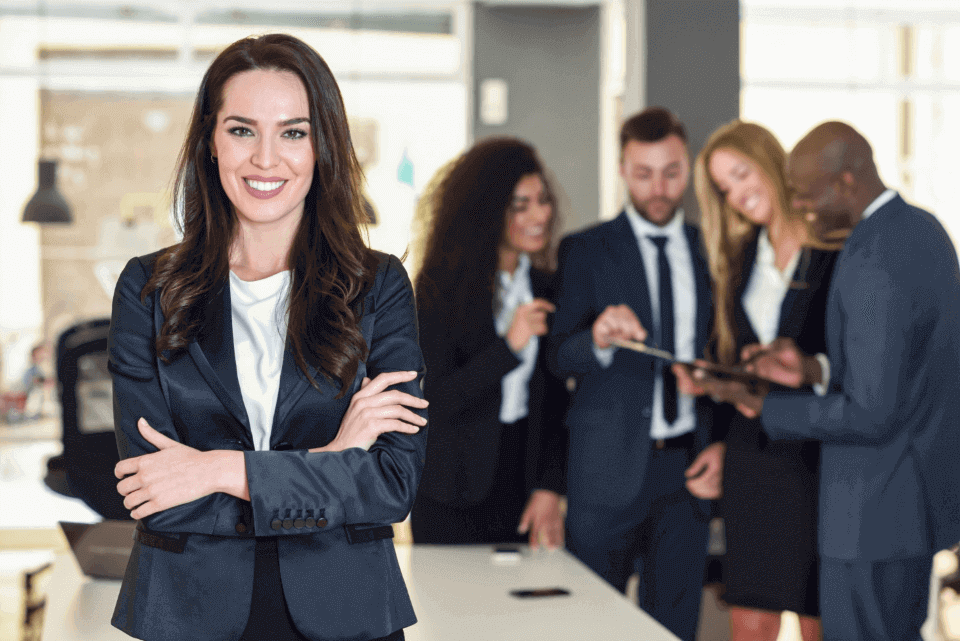 Bussines woman smiling, behind she there are employees watching in a tablet the advantages of 360-degree appraisals