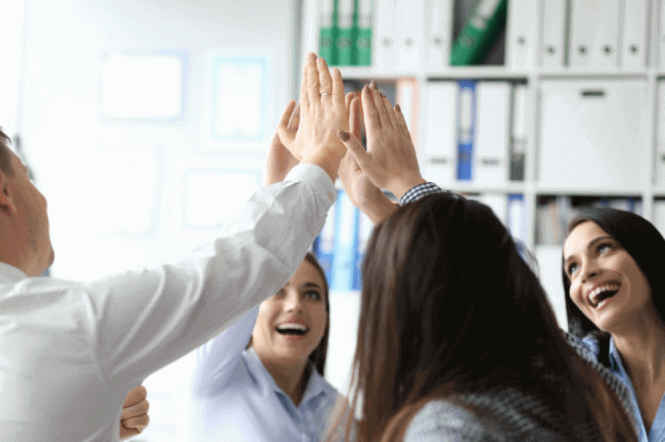 Foto de tres empleadas y un empleado chocando las manos y sonriendo, celebran que lograron a sus objetivos gracias a la medición de kpis